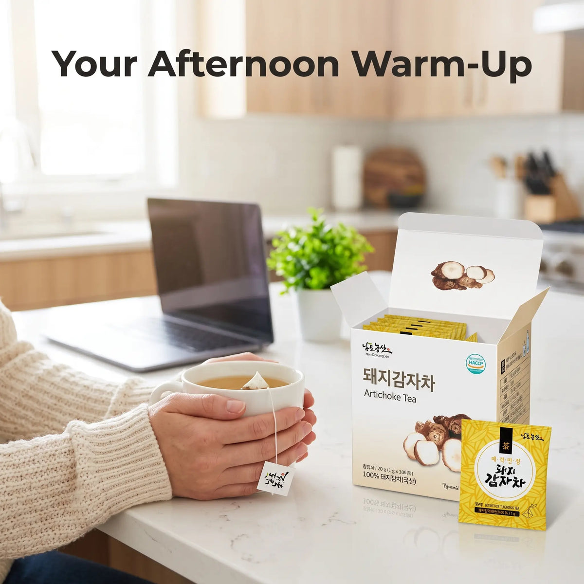 Hands holding a mug of Korean sunchoke tea in a bright kitchen with the tea box beside it