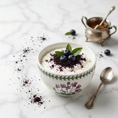 Healthy breakfast bowl with yogurt, fresh blueberries, and Herb & Honey Acai Berry Powder sprinkled on top, placed on a white marble surface.