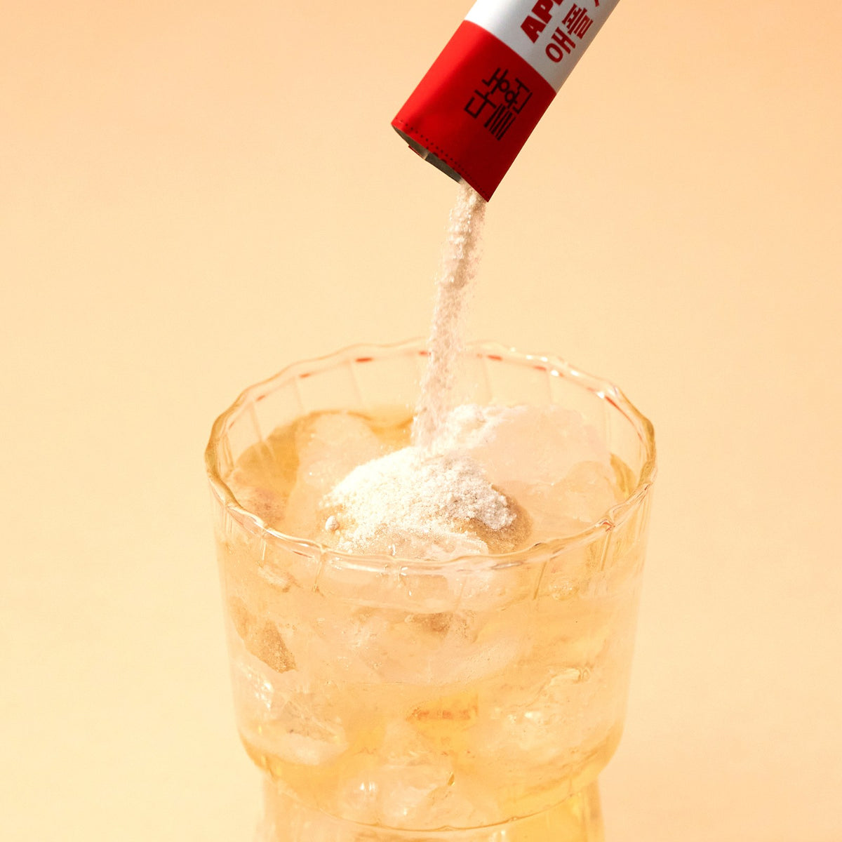 Pouring Korean apple cider vinegar powder from a stick into a glass of ice water