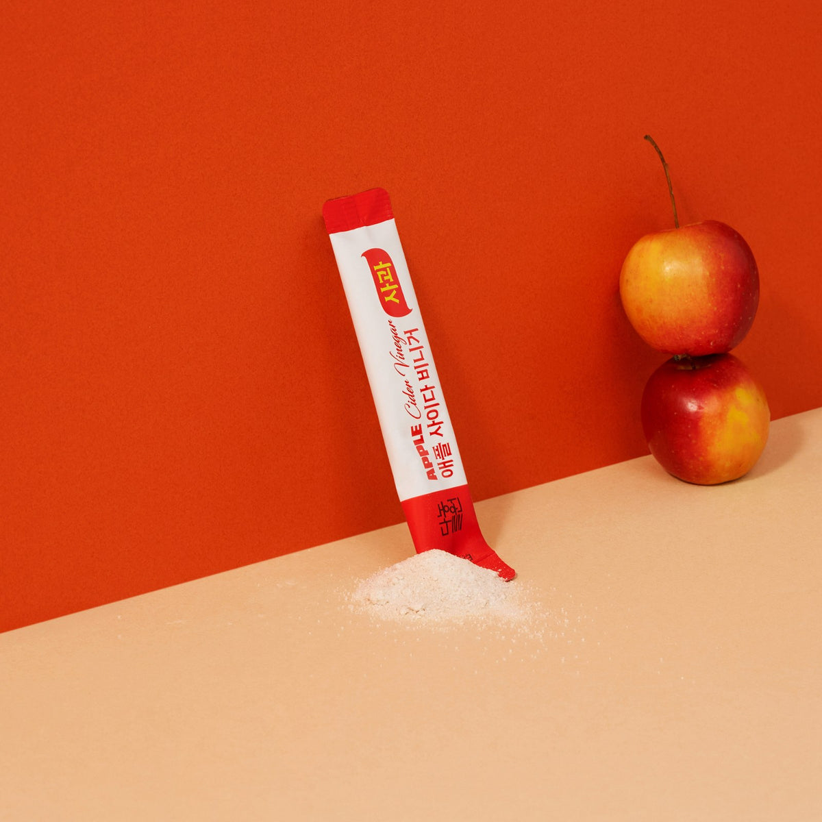 Korean apple cider vinegar powder poured from a stick onto a counter beside two apples