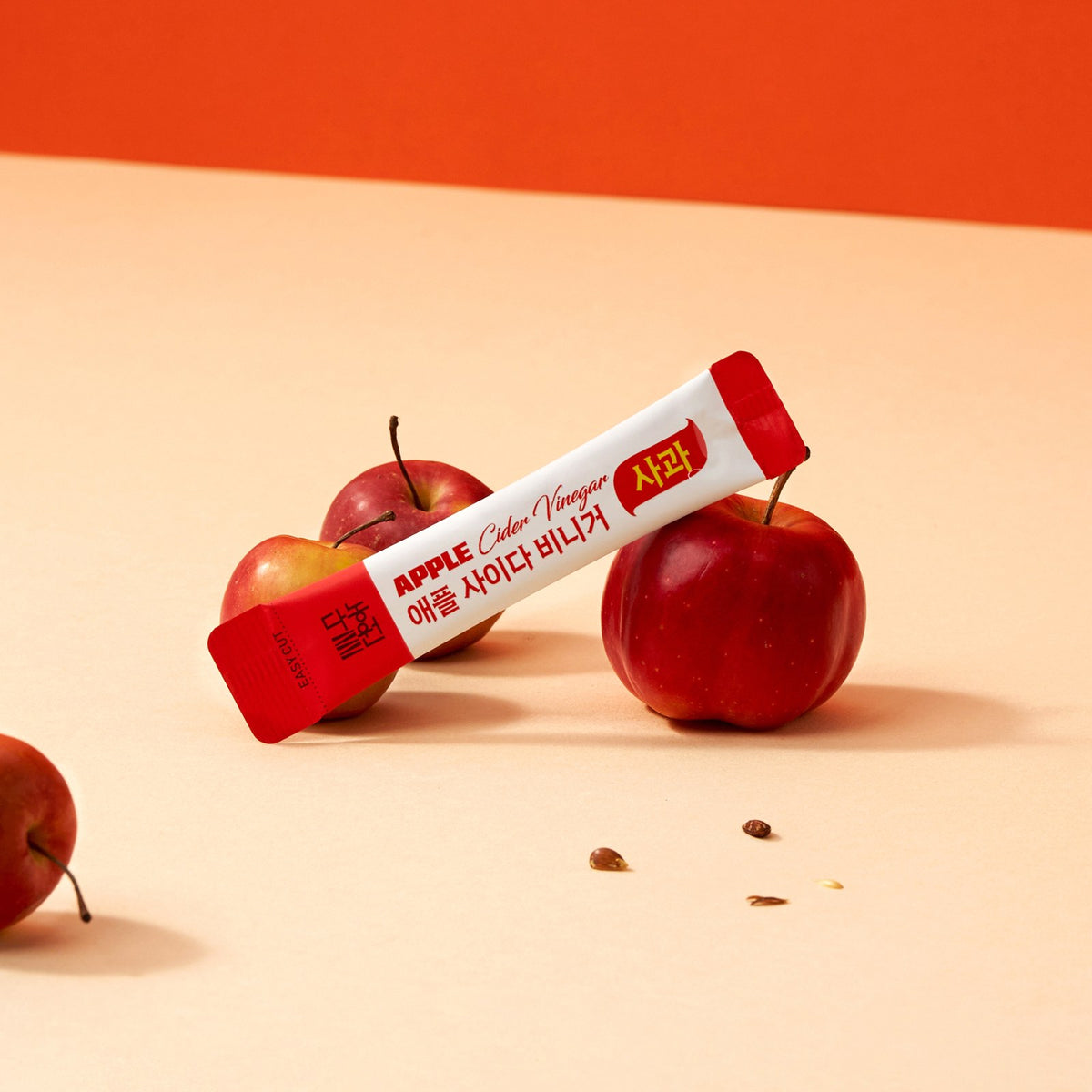 Single Korean apple cider vinegar powder stick, Apple flavor, lying beside fresh red apples