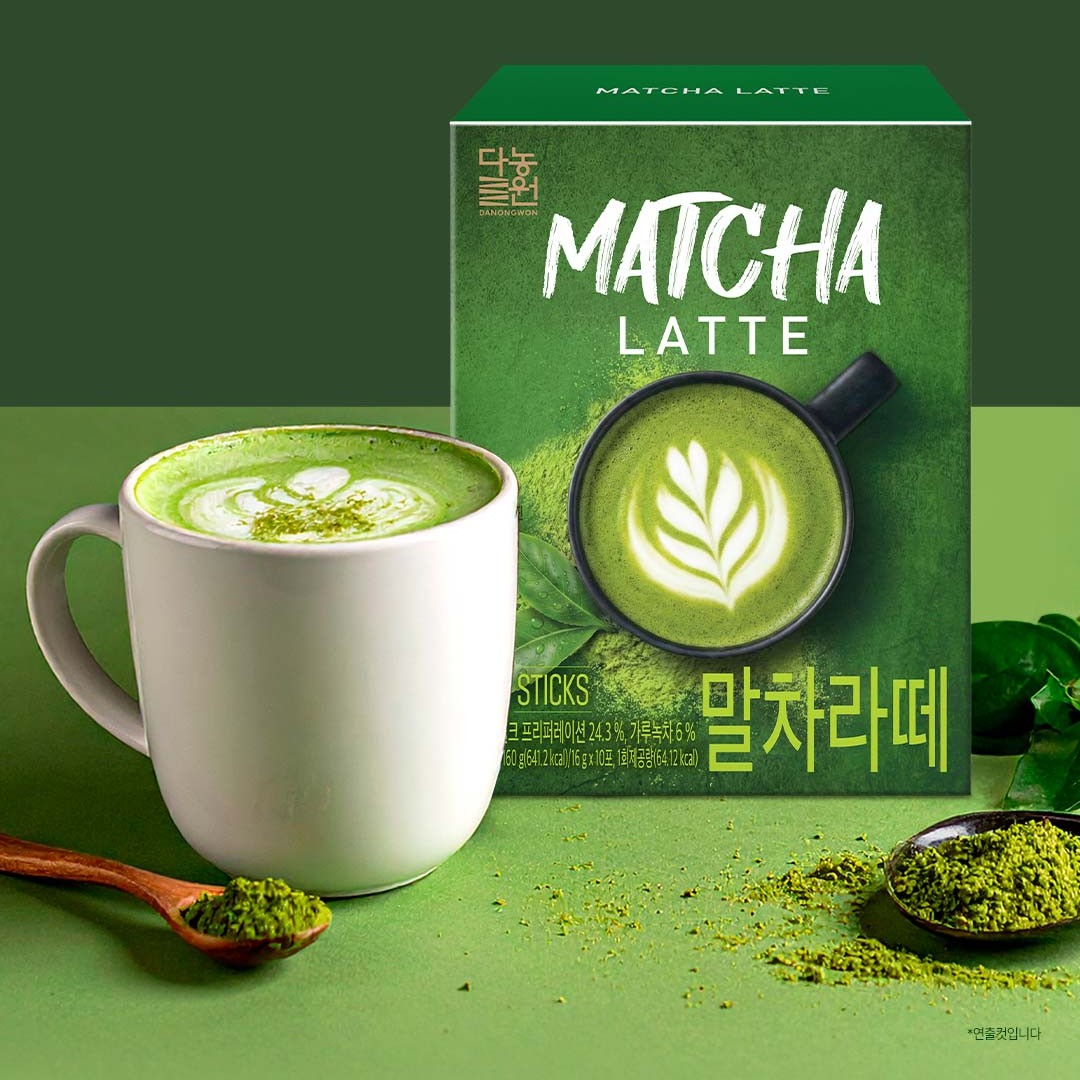Korean matcha latte in a white mug next to the Danongwon matcha latte box and a spoon of green tea powder