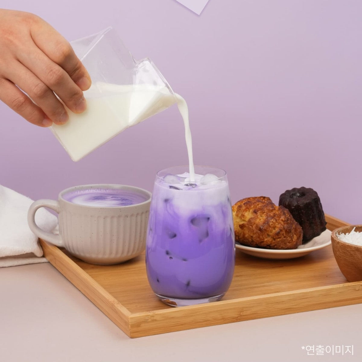 Pouring milk into an iced Korean ube coconut latte on a wooden tray with pastries