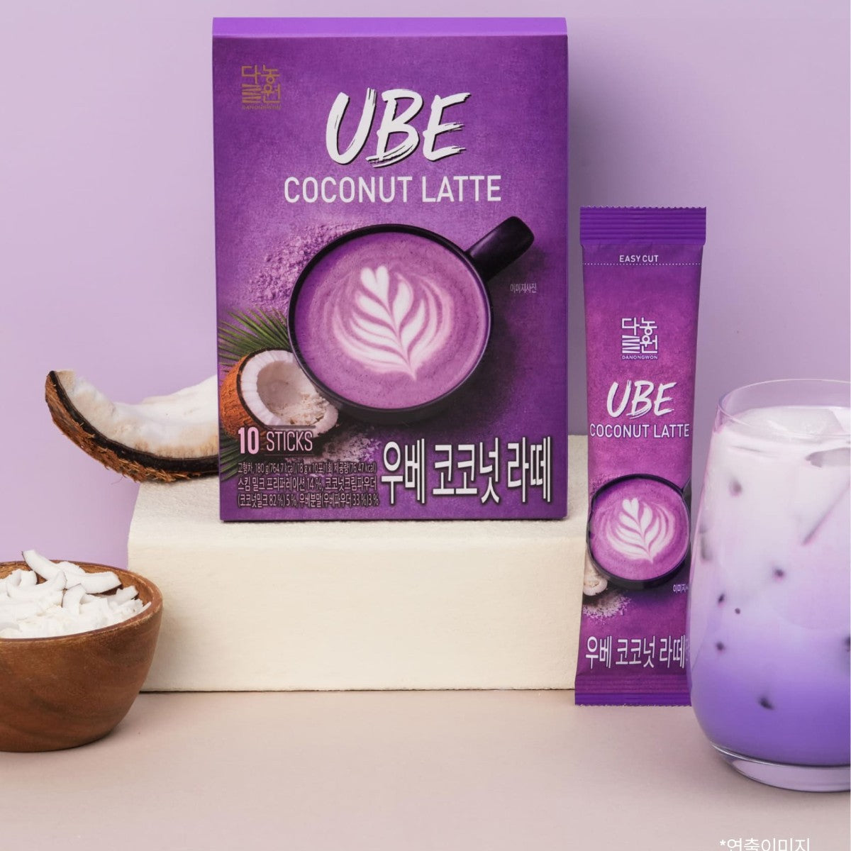 Korean ube coconut latte box and stick beside an iced purple latte and a halved coconut