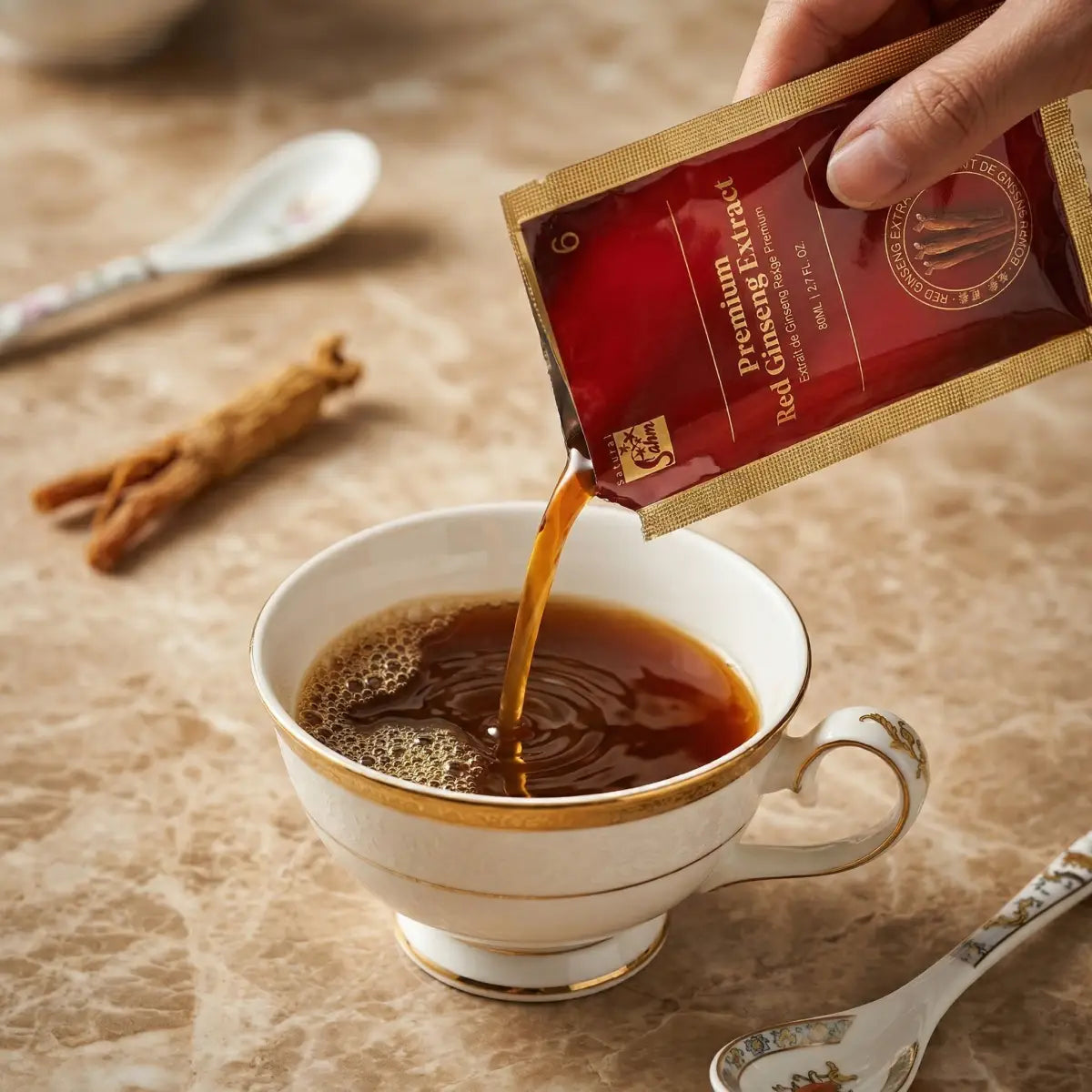 A hand pouring Sahm Canadian Premium Red Ginseng Extract from a pouch into a white tea cup with dried ginseng roots on the side